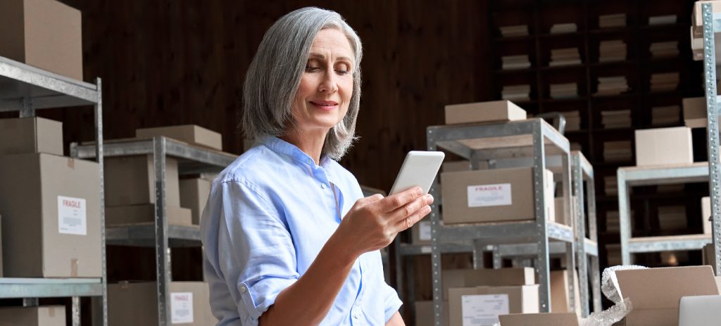 mulher-dentro-de-um-estoque-segurando-celular-para-checar-dados-sobre-a-gestão-de-riscos-no-varejo